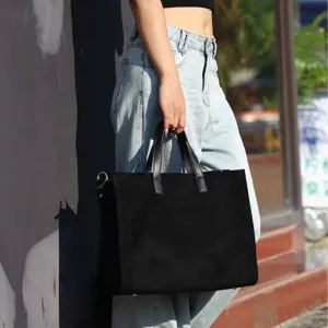 Detailed view of a stylish black suede tote bag held by a model outdoors, elegant.