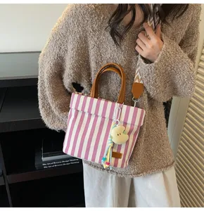 Detail view of pink striped canvas handbag with brown handle, shoulder strap and charm.