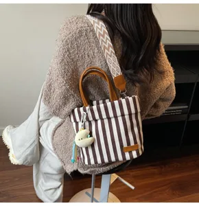 Brown and white striped canvas handbag with wide strap and cute plush pendant for daily commute.