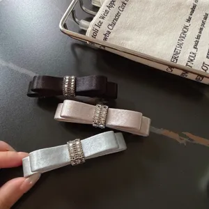 Nahaufnahme eleganter Satinschleifen-Haarspangen mit funkelnden Strass-Zentren in drei Farben.