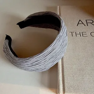 Close-up detail of a wide grey pleated fabric headband styled on a clean minimalist surface.