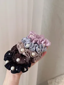 Detailed view of elegant pleated hair scrunchies decorated with pearls, soft fabric design.