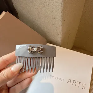 Close-up detail of grey acrylic hair comb featuring elegant pearl and rhinestone bow design.