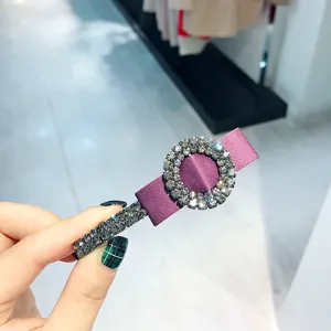 Detailed shot of a purple satin hair clip featuring sparkling rhinestones and metal spring.
