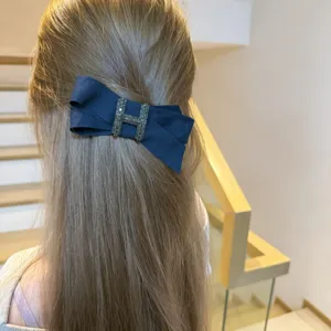 Elegant blue fabric bow hair clip with sparkling rhinestone H centerpiece for women.