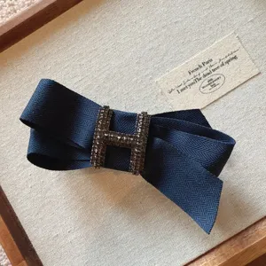 Detailed view of dark blue fabric bow hair clip with rhinestone H buckle, elegant accessory.
