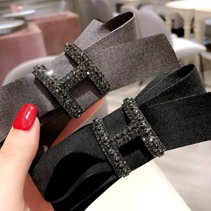 Close-up detail of stylish fabric bow hair clip with sparkling rhinestone H buckle accessory.