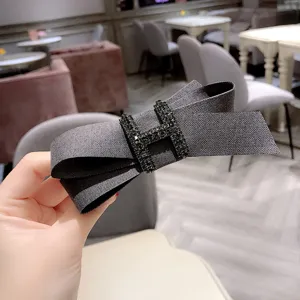 Dark grey herringbone fabric bow hair clip featuring a sparkly rhinestone H centerpiece.
