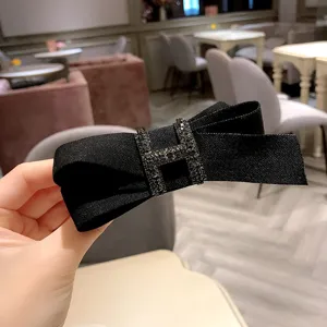 Black fabric bow hair clip with rhinestone H buckle, elegant fashion hair accessory detail.