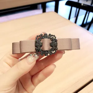 Close-up detail of a taupe satin bow hair clip adorned with a sparkling black rhinestone buckle.