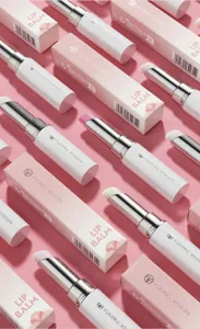 Close up detail of white lip balm tubes and pink packaging boxes arranged neatly on background.