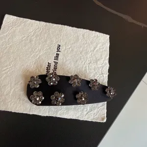 Detail of black satin rhinestone flower hair clip, retro side snap clip for bangs.