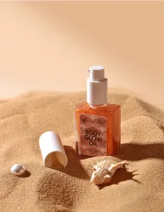 Glanzende lichaamglow-olie in transparante fles met pomp op zandachtergrond voor zomer.