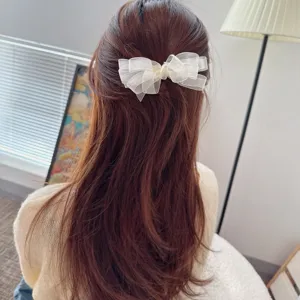 Detail shot of a white sheer organza bow hair clip worn on long brown hair, elegant accessory.