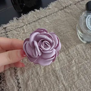 Purple fabric camellia brooch and hair accessory detail shot, elegant floral design.