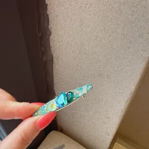 Primo piano dettagliato della forcina per capelli con strass e cristalli blu e verdi.