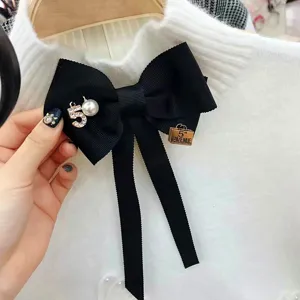 Detailaufnahme einer schicken schwarzen Schleifenbrosche mit Strass-Zahl 5 und Perlenanhängern.