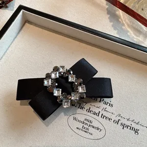 Detailed shot of black satin bow hair clip featuring sparkling rhinestone crystal buckle.
