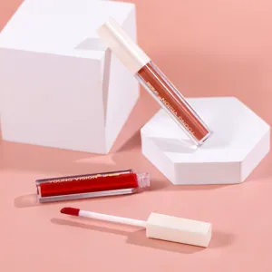 Lip gloss detail shot showing texture, dual tubes, and applicator brush in studio setting.