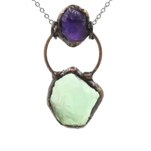 Close-up of vintage raw crystal pendant with purple and green stones and copper setting details.