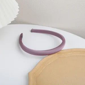 Detail shot of a sleek purple satin headband on a clean white tabletop with minimalist props.