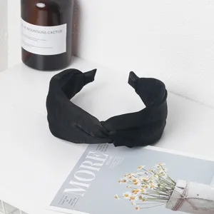 Primer plano detallado de una diadema negra de tela con nudo sobre un fondo blanco liso.