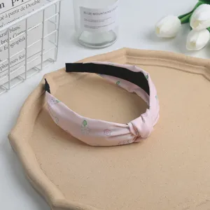Pink knotted fabric headband with cute floral print, stylish hair accessory close-up detail.