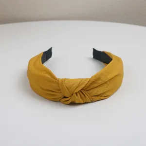 Close-up view of a mustard yellow fabric knotted hairband showing textured fabric details.