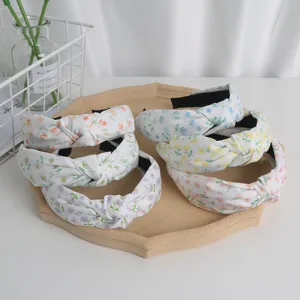 Detailed view of floral printed wide knotted headbands on a wooden tray with green decor.