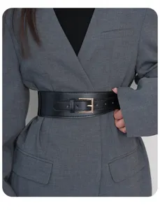 Detailed view of wide black leather waist belt with gold buckle worn over grey blazer jacket.