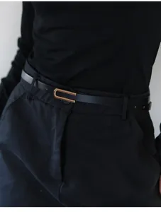 Close-up of a stylish black slim belt with a metallic gold buckle worn on pants detail shot.