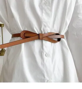 Detail shot of a brown thin leather belt worn over a white shirt, stylish waist accessory.