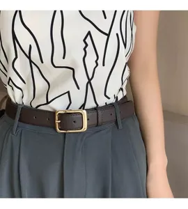 Close-up detail of a stylish brown leather belt with a gold square buckle worn on trousers.