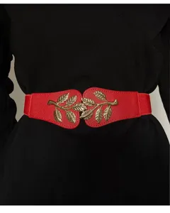 Gros plan d'une ceinture élastique rouge avec boucle de feuille dorée sur robe noire.