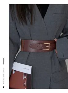 Detail view of a wide brown leather belt with elastic band and gold metal buckle for women.