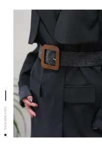 Detail shot of the wide elastic belt with a wooden square buckle worn on a black coat.