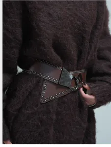 Detail view of the punk style wide leather belt with rivets, metal ring and asymmetric design.