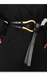 Dettaglio ravvicinato della cintura da donna in pelle nera con grande fibbia dorata a ferro di cavallo.