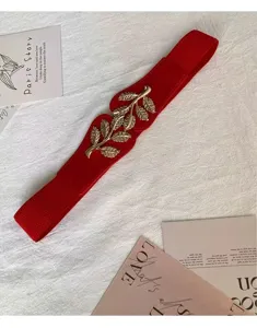 Détail de ceinture élastique rouge avec boucle de feuille dorée pour robe élégante.