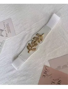 Gros plan sur la ceinture élastique à boucle feuille dorée, accessoire de robe élégant.