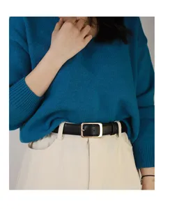 Close-up detail of a minimalist black leather belt with a gold square pin buckle worn on trousers.