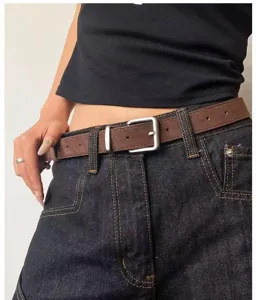Close-up view of a brown vintage thin belt worn with dark jeans, showing metal buckle detail.