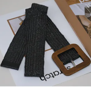 Detailed view of a black woven wide belt with a large wooden square buckle, casual design.