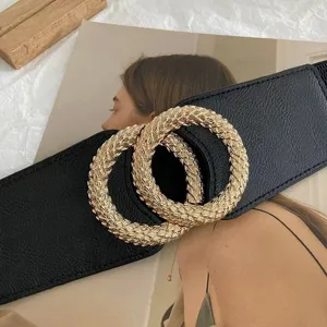 Wide black elastic waist belt for women with interlocking gold rings, perfect for coat styling.