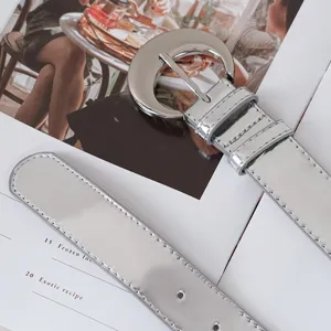 Silver glossy women's leather belt with metallic round buckle for dresses and jeans.