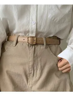 Detail view of a stylish tan leather belt featuring a chic gold twist square buckle.