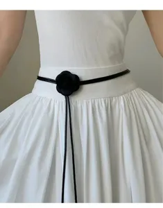 Primer plano de un cinturón negro fino y elegante con detalle de flor de camelia.