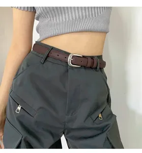 Close-up view of a stylish brown leather belt featuring a silver metal buckle on dark pants.