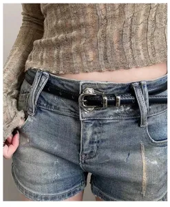 Close-up view of a sleek black thin leather belt with vintage silver buckle on jeans.