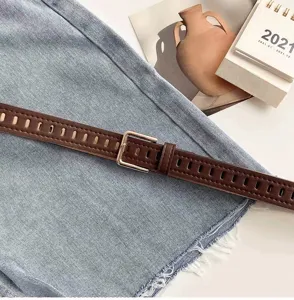 Close-up of brown perforated leather belt with metal buckle on light blue denim fabric.